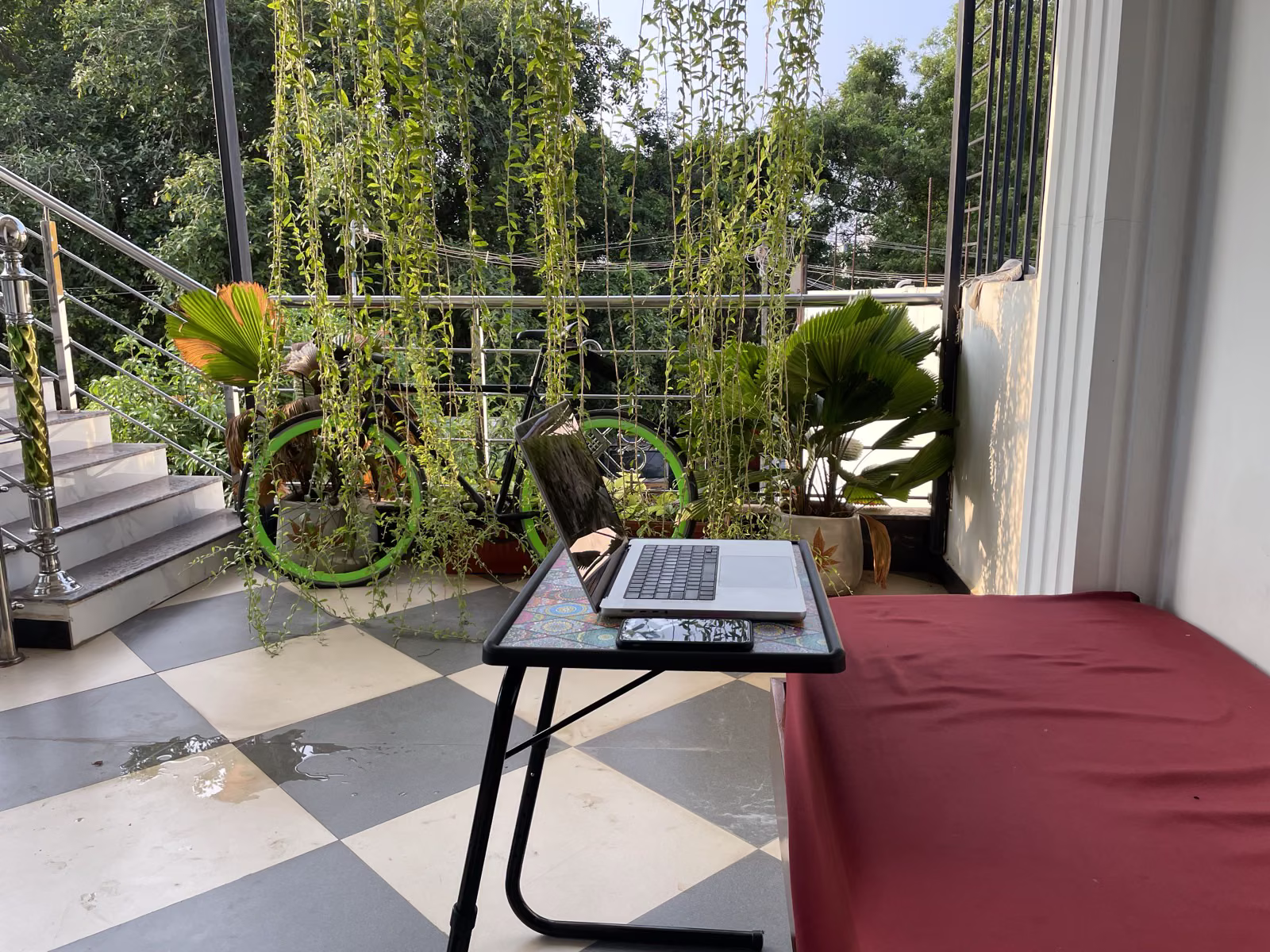MacBook on an adjustable laptop stand on the Nivaa Stays balcony, surrounded by hanging vines